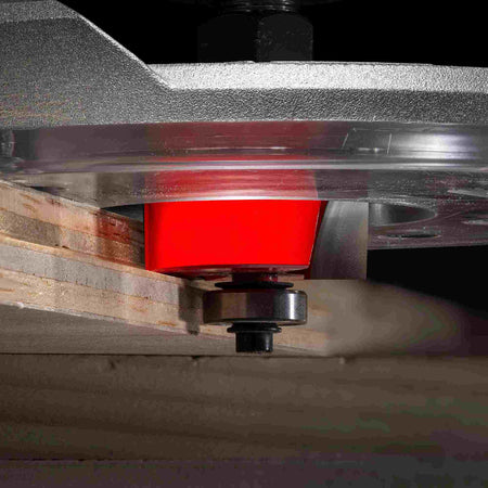 A close-up action photograph of the Freud 32-522 bit mounted in a router table, performing a clean rabbeting cut on the edge of a piece of plywood.