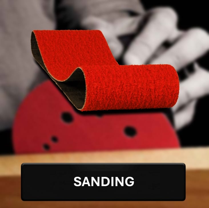 Red sanding block on a wooden surface with blurred hands in the background, labeled 'SANDING'.