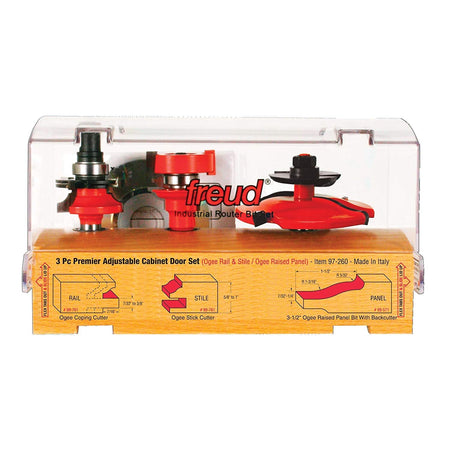 This is a clear plastic case containing a set of three red and silver router bits, designed for woodworking, displayed on a wooden base. The base has labels and diagrams illustrating the profiles created by each of the "3 Pc Premier Adjustable Cabinet Door Set" components: an Ogee Coping Cutter, an Ogee Stick Cutter, and a 3-1/2" Ogee Raised Panel Bit with Backcutter.