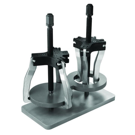 Image of GearWrench 2 & 5 Ton 2 or 3 Jaw Internal/External Ratcheting Puller Set. The image shows two silver and black mechanical pullers, tools used for removing parts, standing on a flat metal base. Each tool has a central threaded rod and three curved jaws that grip a circular plate, creating a setup for applying force to remove a part.