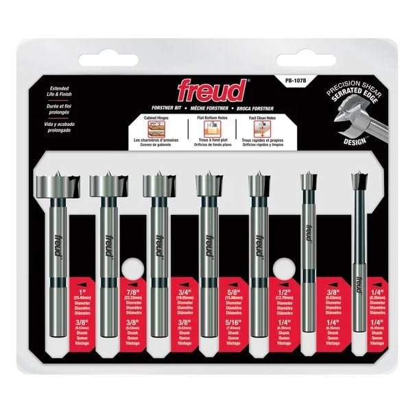 Forstner bit set in packaging. 
This is a retail image of a Freud 7-piece Forstner bit set, model PB-107B, presented in clear blister packaging on a white and black card. The seven silver-colored bits, ranging in size from 1/4-inch to 1-inch, are arranged horizontally, each with its size and shank diameter clearly labeled below it.